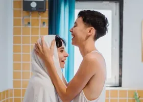 Dwie uśmiechnięte kobiety w łazience. Jedna z nich wyciera ręcznikiem drugą.